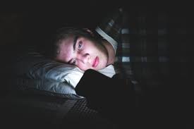 A person lying in bed at night lit only by their phone screen